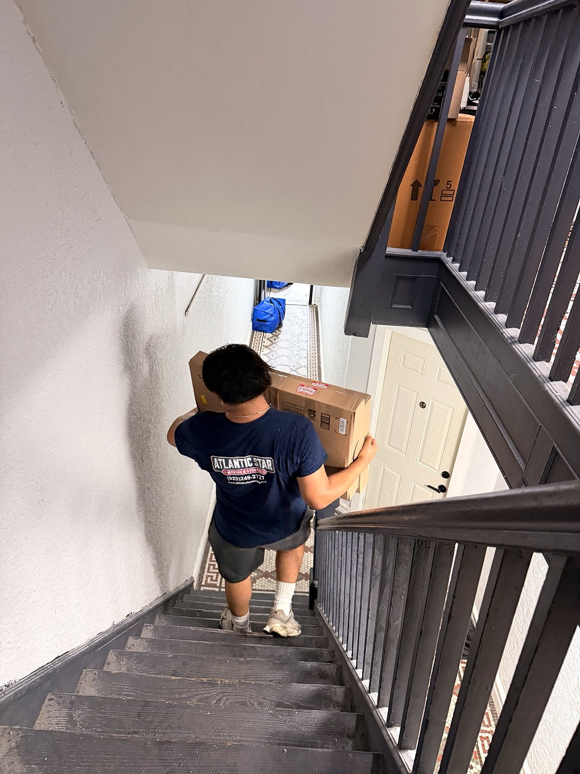 Atlantic Star mover carrying a moving box down an apartment stairway